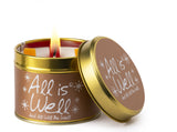 Lily-Flame All is Well scented tin candle with a decorative label and metal lid, emitting a warm, inviting glow.
