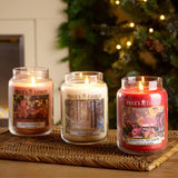 Large glass jar candle with a magnolia fragrance from Price's Candle, featuring a clear container and a lit wick.