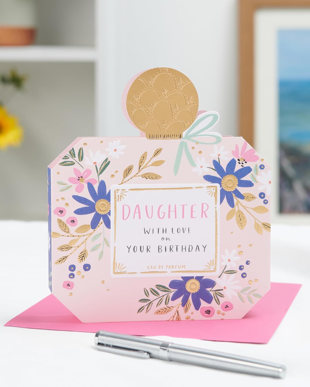 UK Greetings birthday card for daughter featuring a perfume bottle-shaped design with floral accents and colorful illustrations.